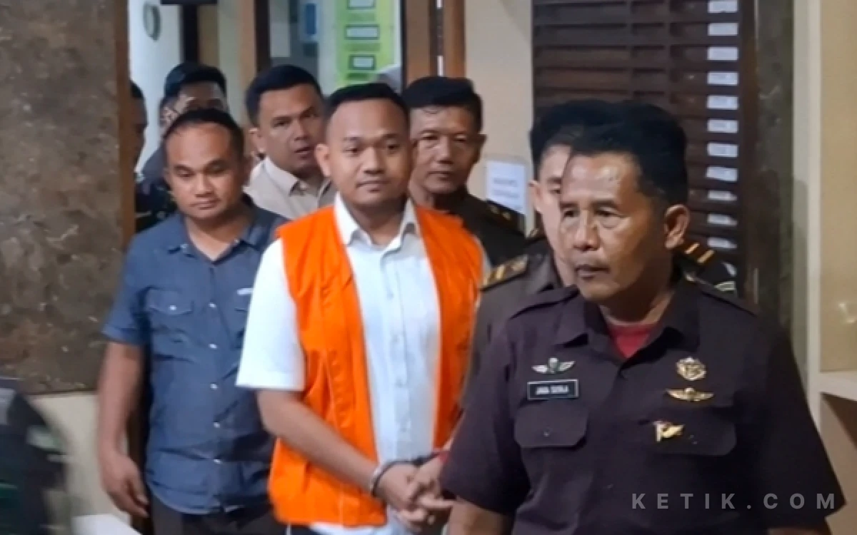 Foto Anggota DPRD Kabupaten Sleman, Raudi Akmal (rompi oranye), berjalan dengan tangan terborgol dan dikawal oleh petugas Kejari Sleman dan personel keamanan setelah resmi ditetapkan sebagai tersangka, Senin malam 22 Juni 2026. (Foto: Fajar R/Ketik.com)
