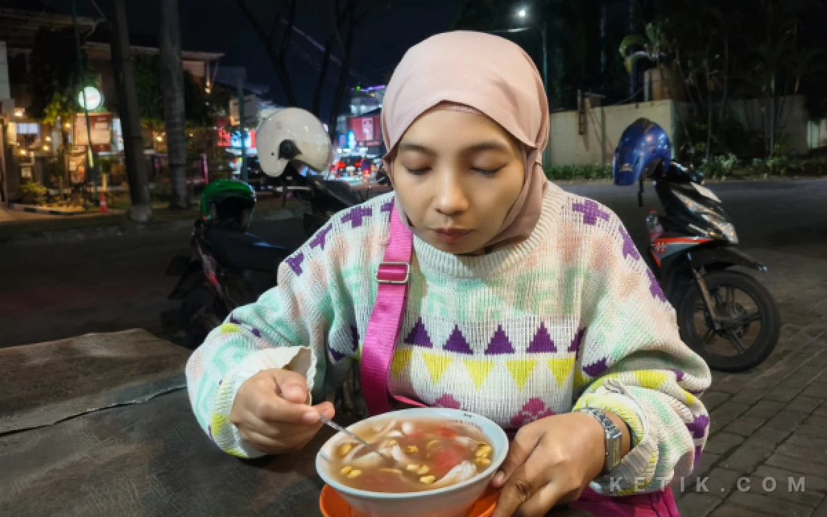 Foto Bu Ni'mah menikmati ronde hangat di depan Kedai Ronde Angsle LA "Cak Man", di Delta Sari pada Selasa malam, 18 Agustus 2026. 
(Charleen Alexa Putri Pratama/ketik.com)